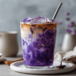 Close-up of an iced ube coconut latte in a clear glass, showing creamy purple layers with espresso and ice.