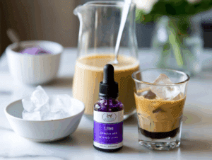 Flat lay of modern ingredients for iced ube coconut latte, including coconut milk, ube extract, espresso, oat milk, and ice on marble.